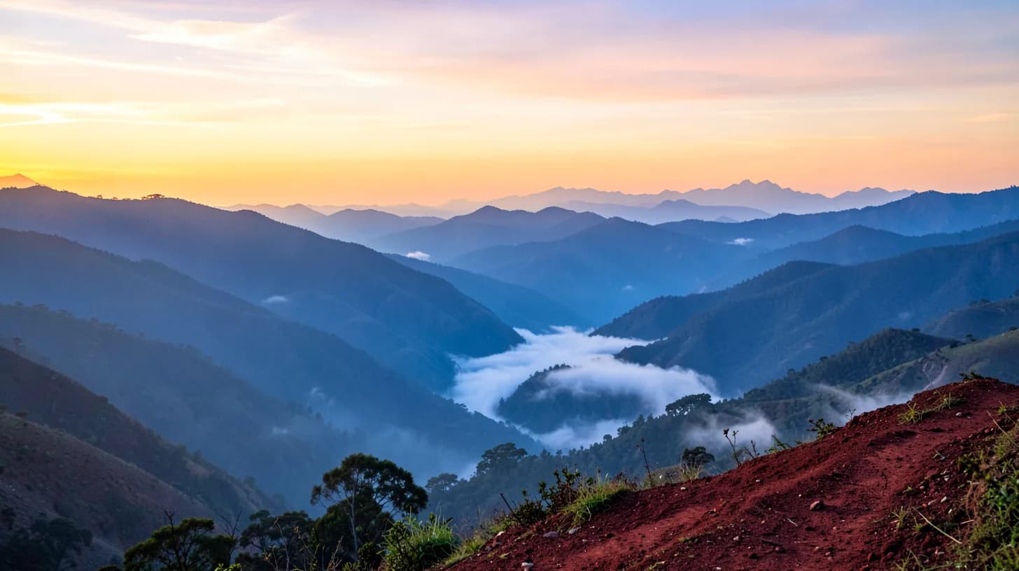 Wide view of misty Andean ridges at sunrise in Huila, with a tiny distant figure on a red earth trail.