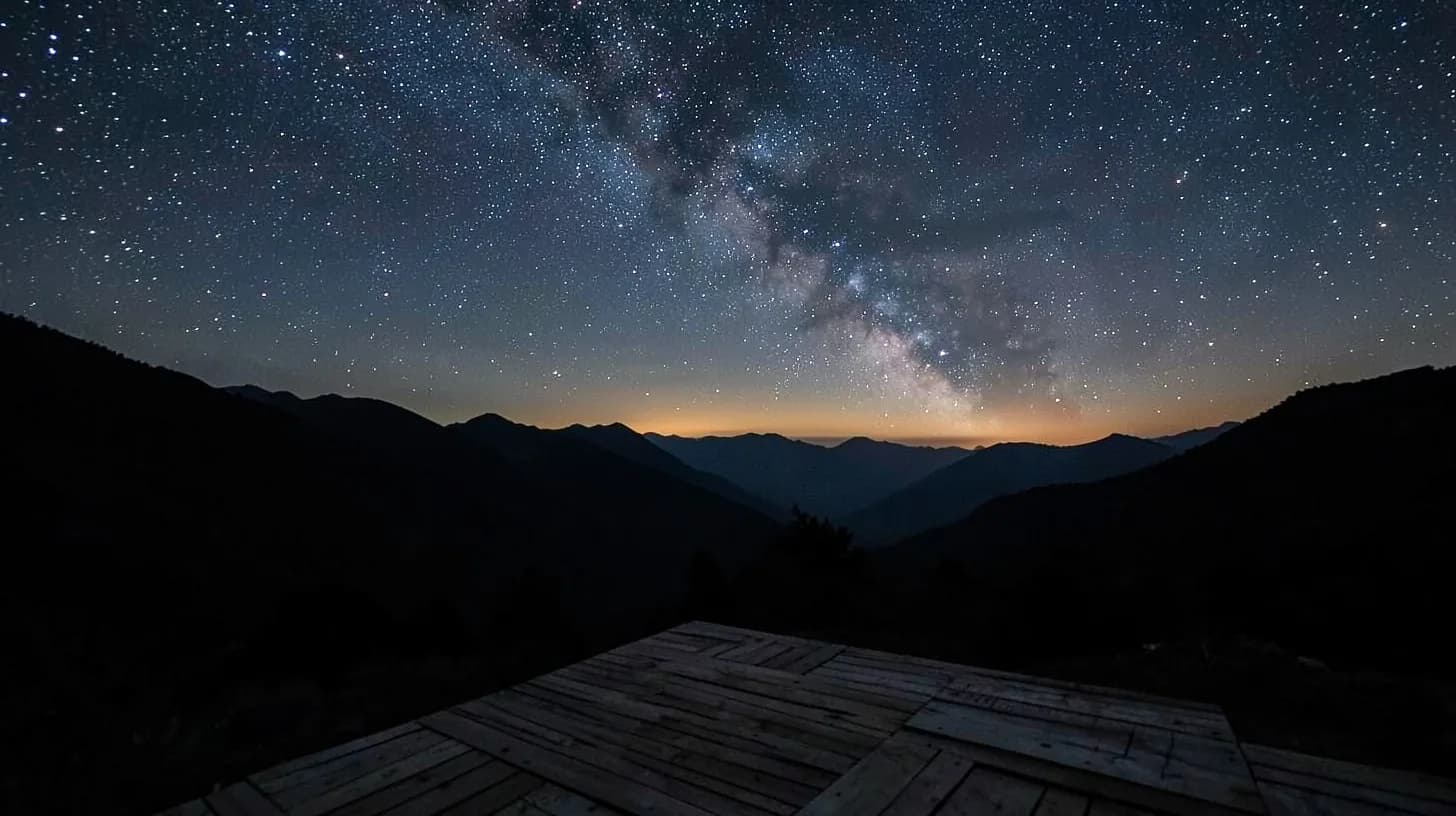 The Milky Way arching over the silhouetted ridges of an Andean valley, a simple unfinished timber deck platform in the dark foreground.